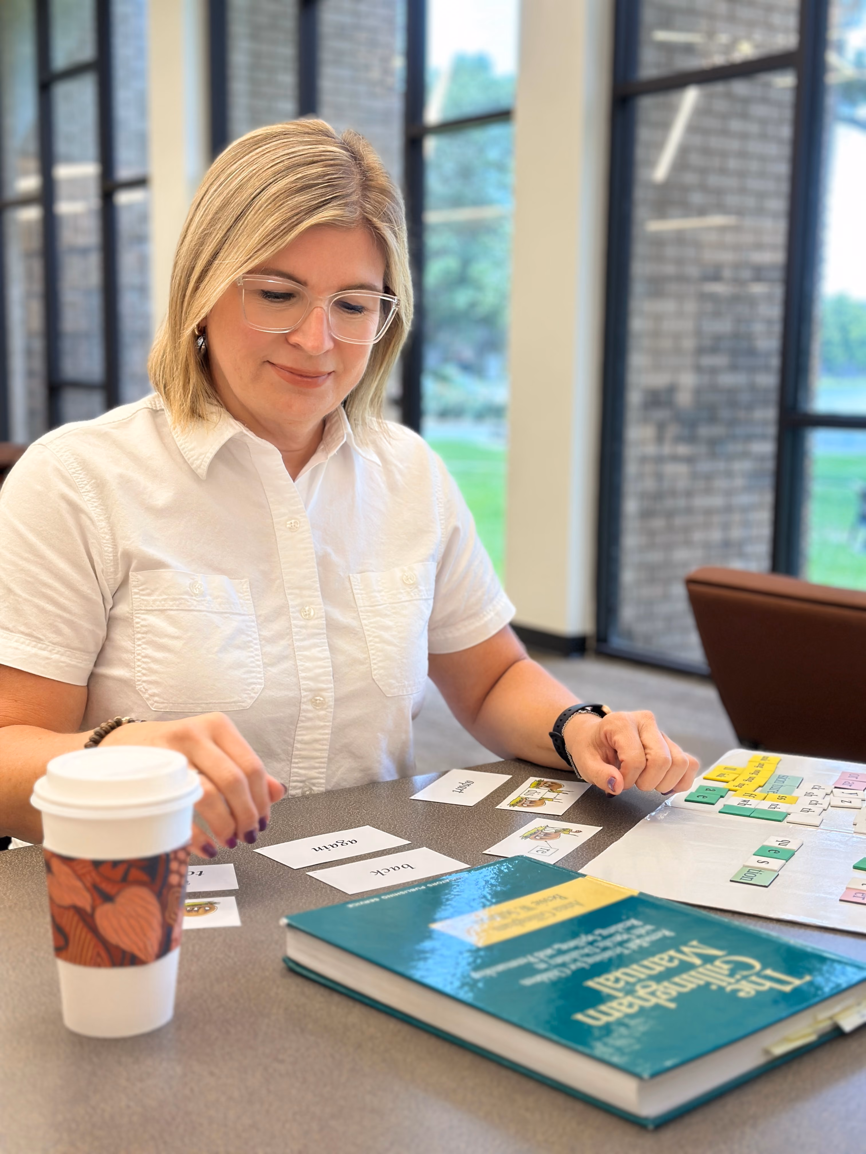 Kristine Carew arranging word cards and phoneme tiles on a table beside
The Gillingham Manual during an Orton-Gillingham tutoring session.
