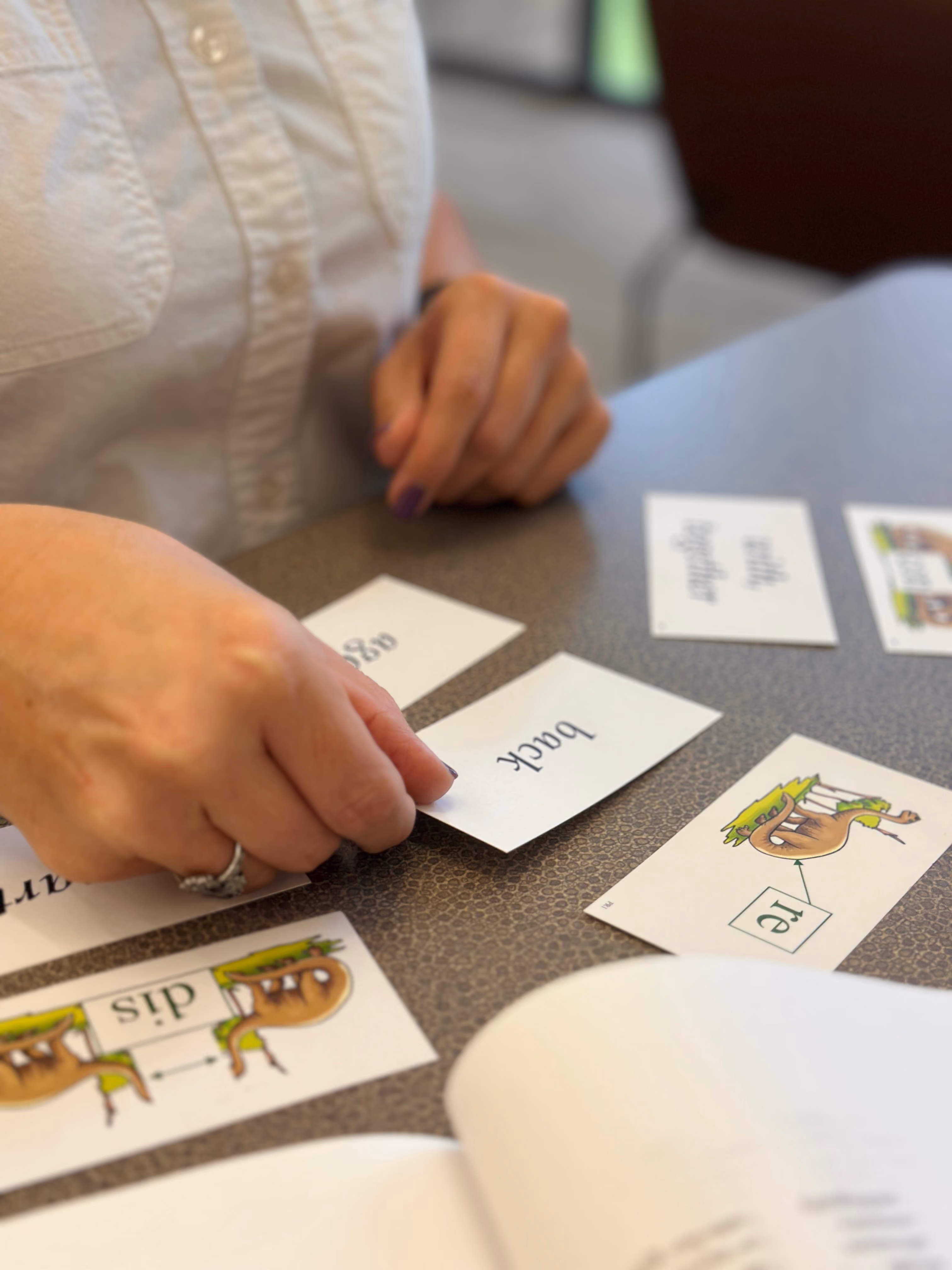 Hands matching prefix cards for "dis" and "re" with meaning cards reading "back," "again," and "with, together" during an Orton-Gillingham morphology lesson.