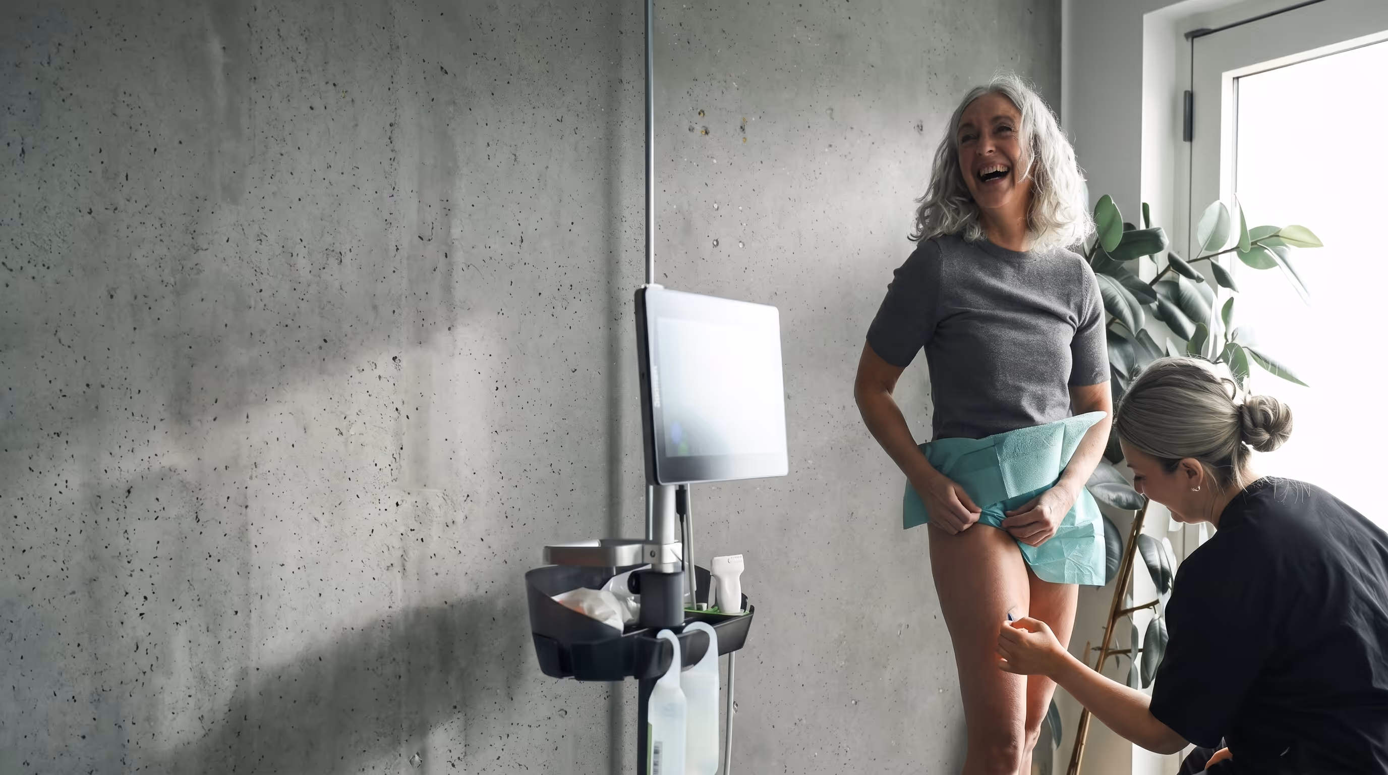 Woman smiling during a medical ultrasound exam of her upper thigh by a healthcare professional.