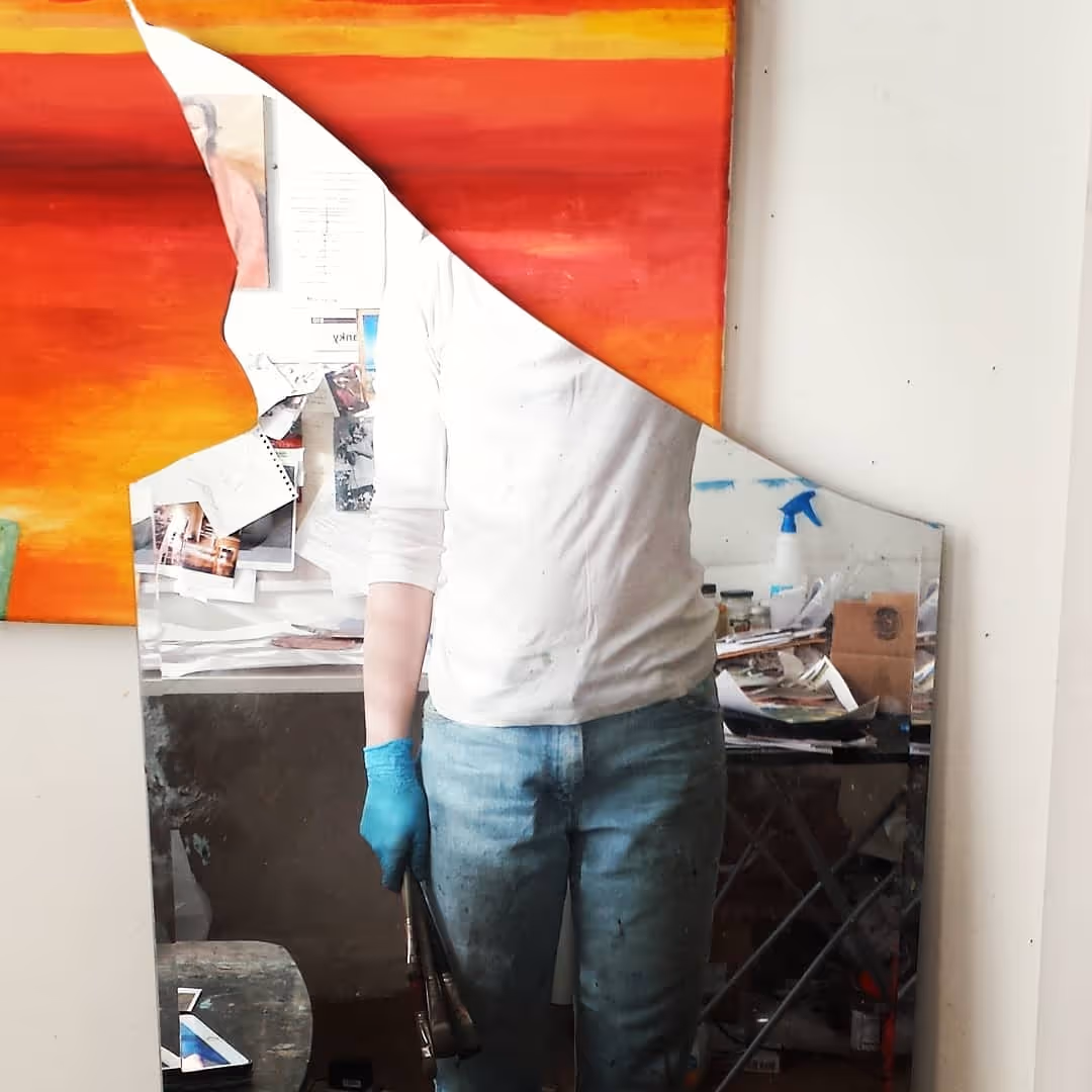 The artist stands in her studio in front of a broken mirror. We a bit of her studio space, including inspiration image, and painting supplies.