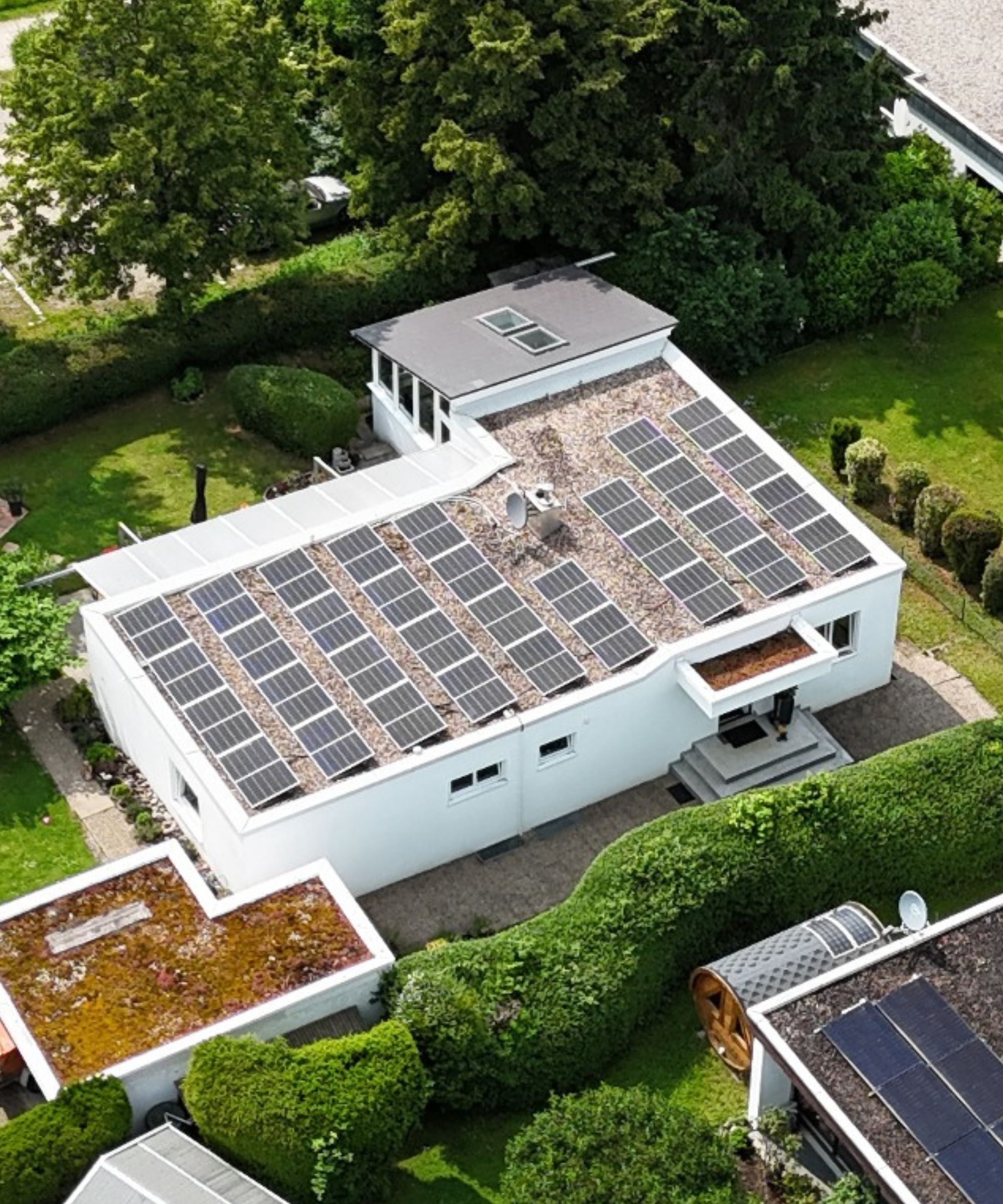 Ein Luftbild eines Hauses mit einem Flachdach, das mit einer großen Anzahl von Solarpanelen ausgestattet ist. 