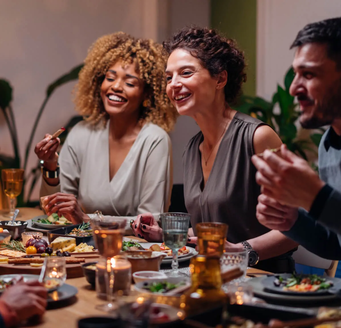 Een groep vrienden geniet van een gezellig etentje bij kaarslicht. Ze zitten rond een tafel vol met diverse gerechten en drankjes, en praten lachend met elkaar.