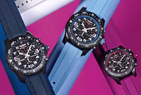 Three black Breitling watches with blue and purple rubber straps on a bright purple background.