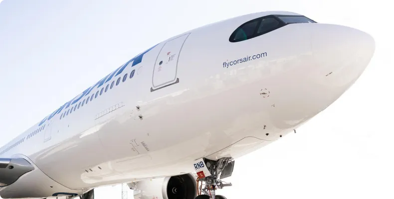 Close-up of the nose and cockpit of a white Corsair airplane with the website flycorsair.com visible under the cockpit window.
