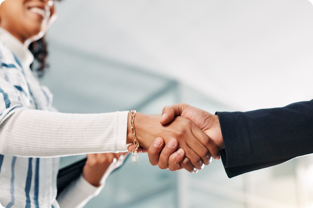 Two people shaking hands in a professional setting, one wearing a white sweater and gold bracelet.