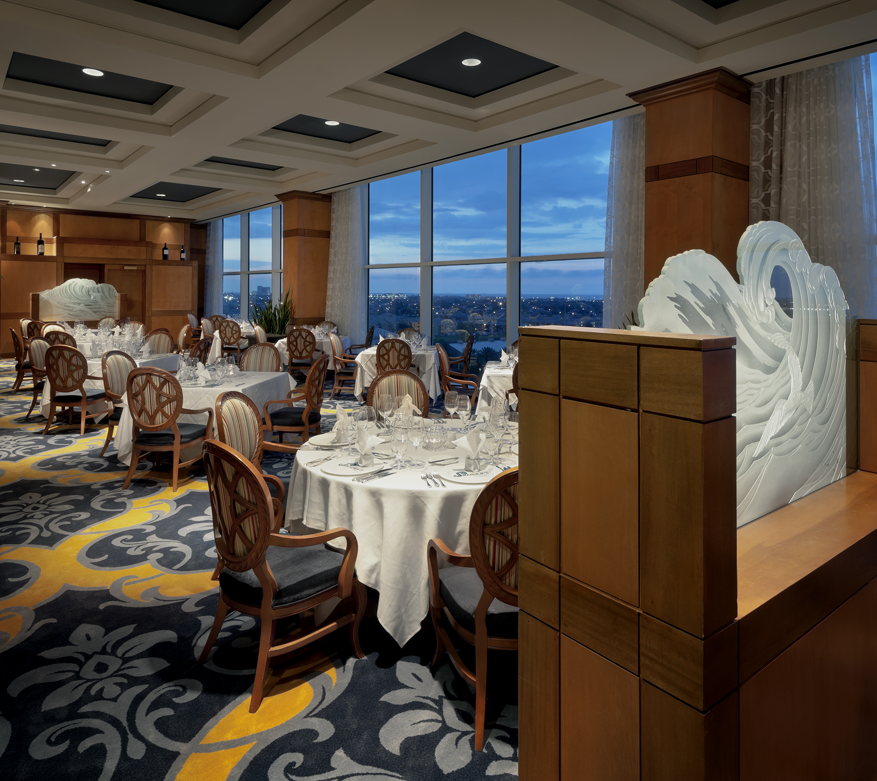 Tables set for dinner beside the sculpted wave wall and Gulf-view windows in Shearn's dining room