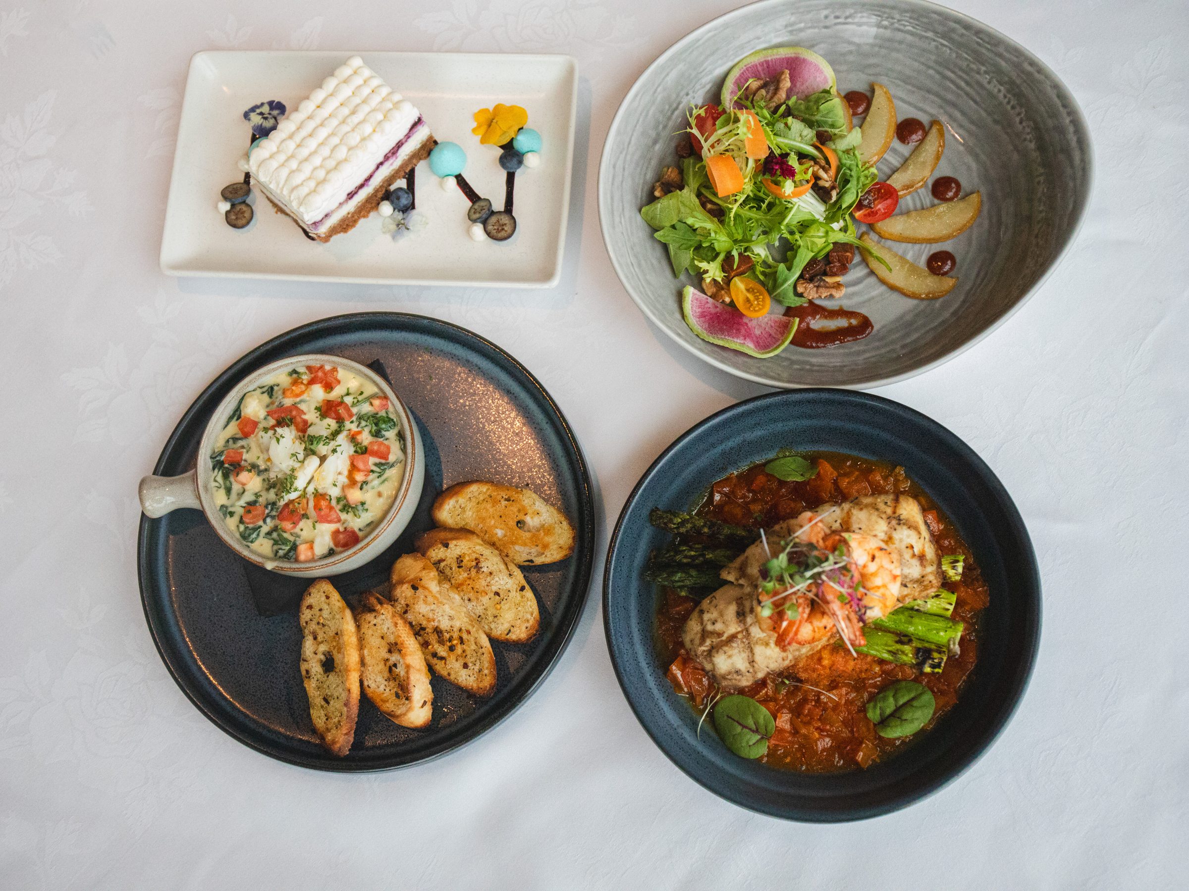 Shearn's appetizers, salad, seafood entree, and dessert on a white tablecloth