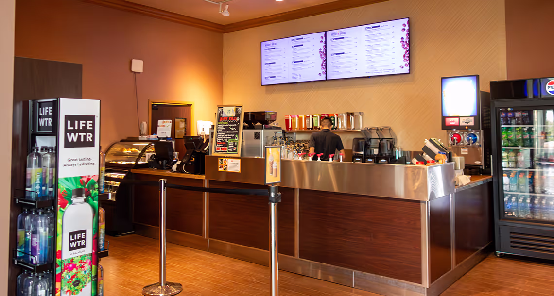 The counter inside Moody Brews at Moody Gardens Hotel, with a barista preparing drinks under the menu board