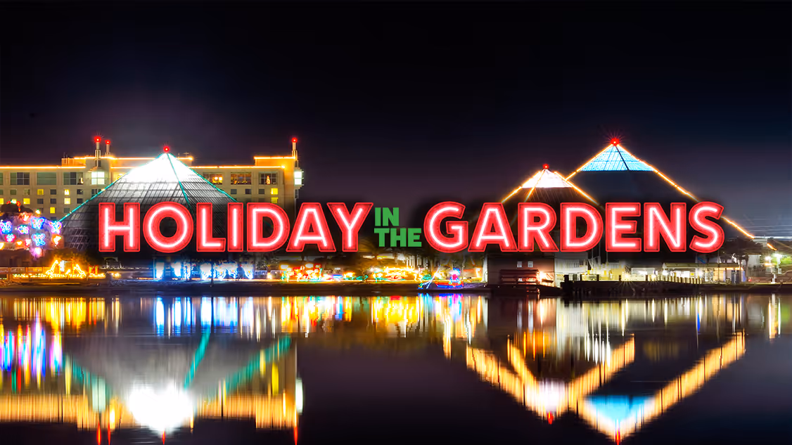 Holiday in the Gardens sign over the Moody Gardens pyramids lit for the season and reflected in the water