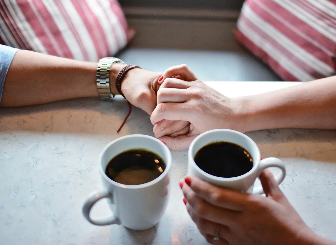 two people holding hands over two cups of coffee