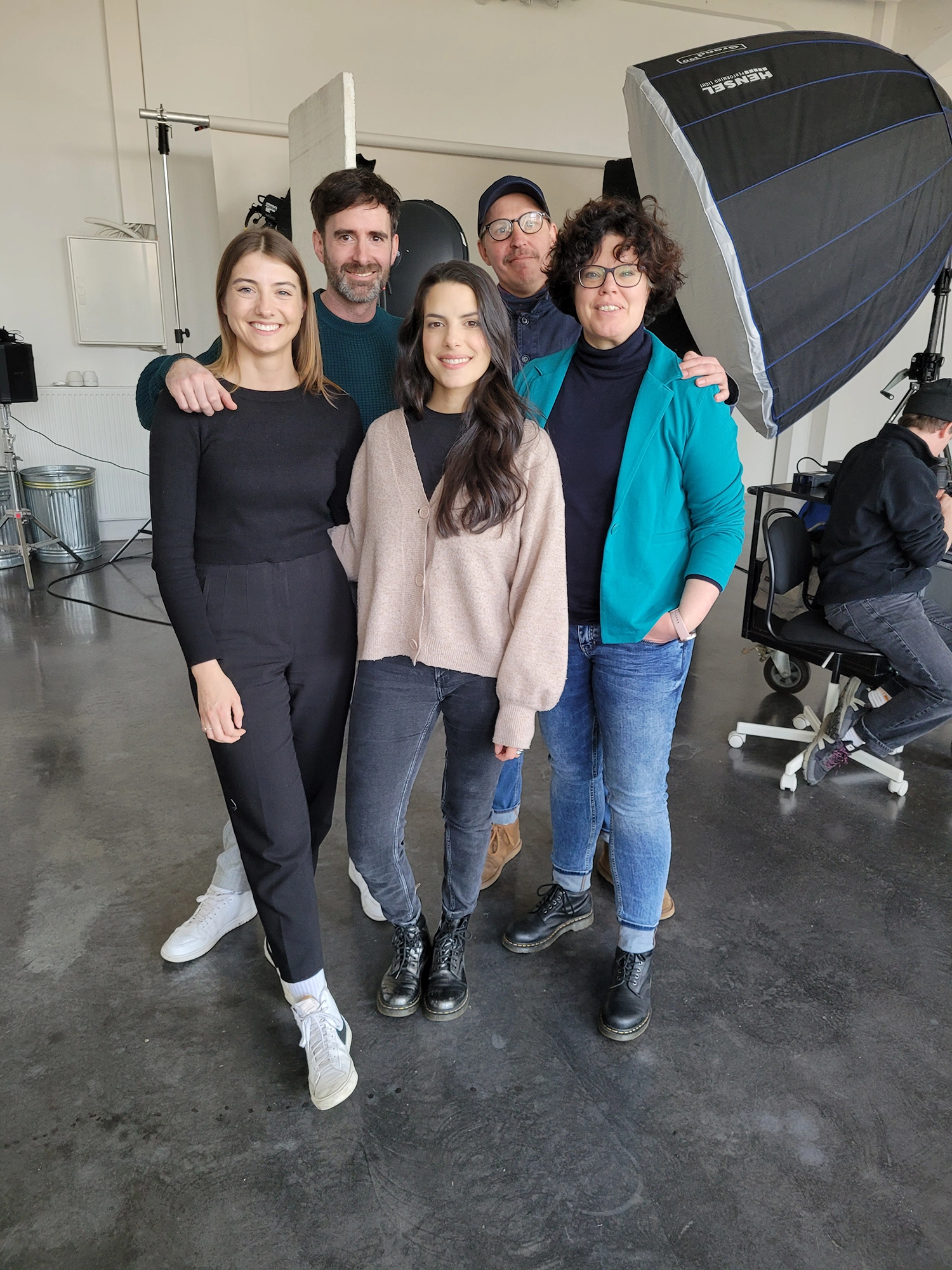 Fünf lächelnde Personen stehen eng zusammen in einem Fotostudio mit professioneller Beleuchtung.