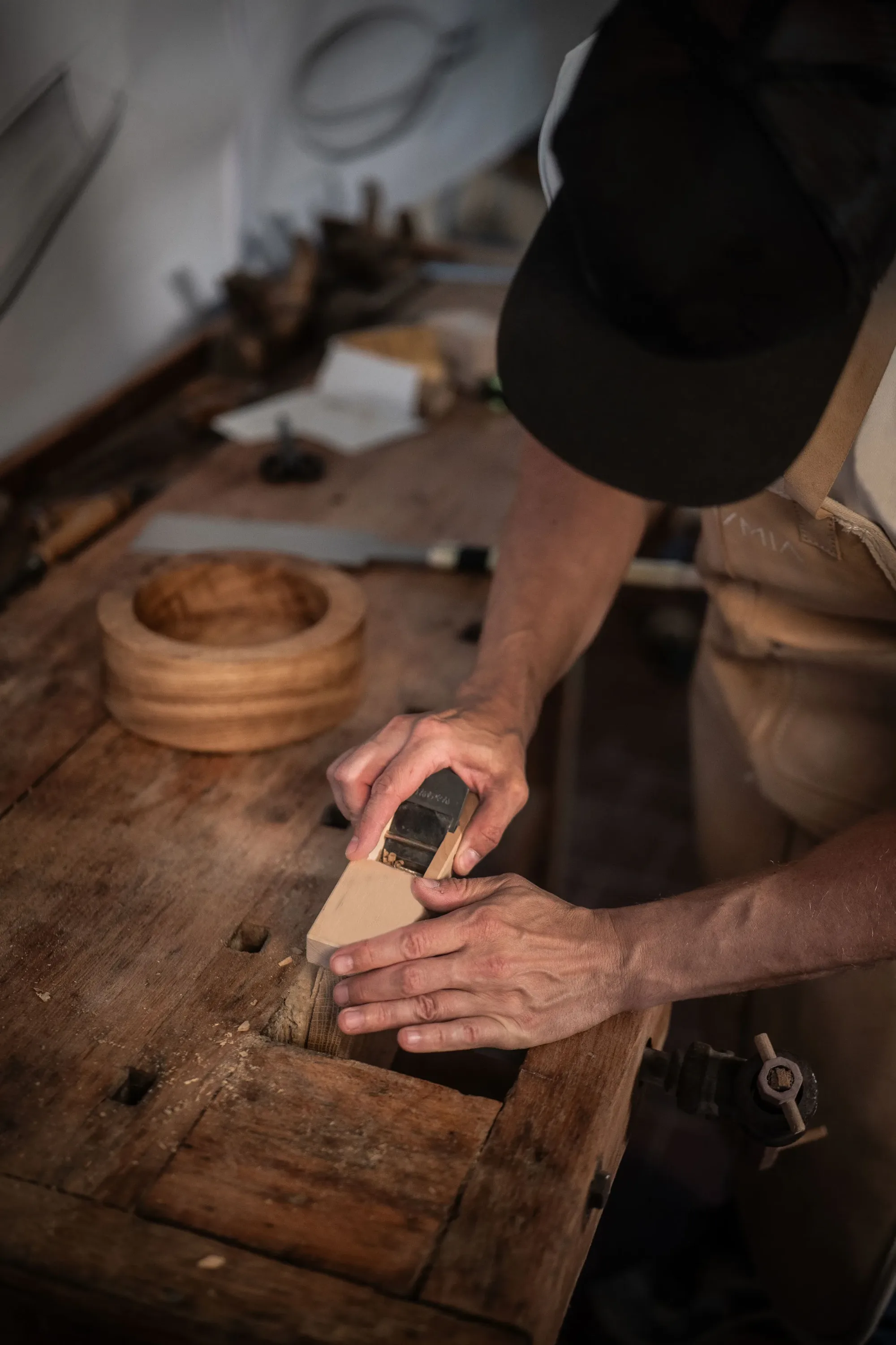 Planing a small curved piece, a round wooden bowl on the bench behind