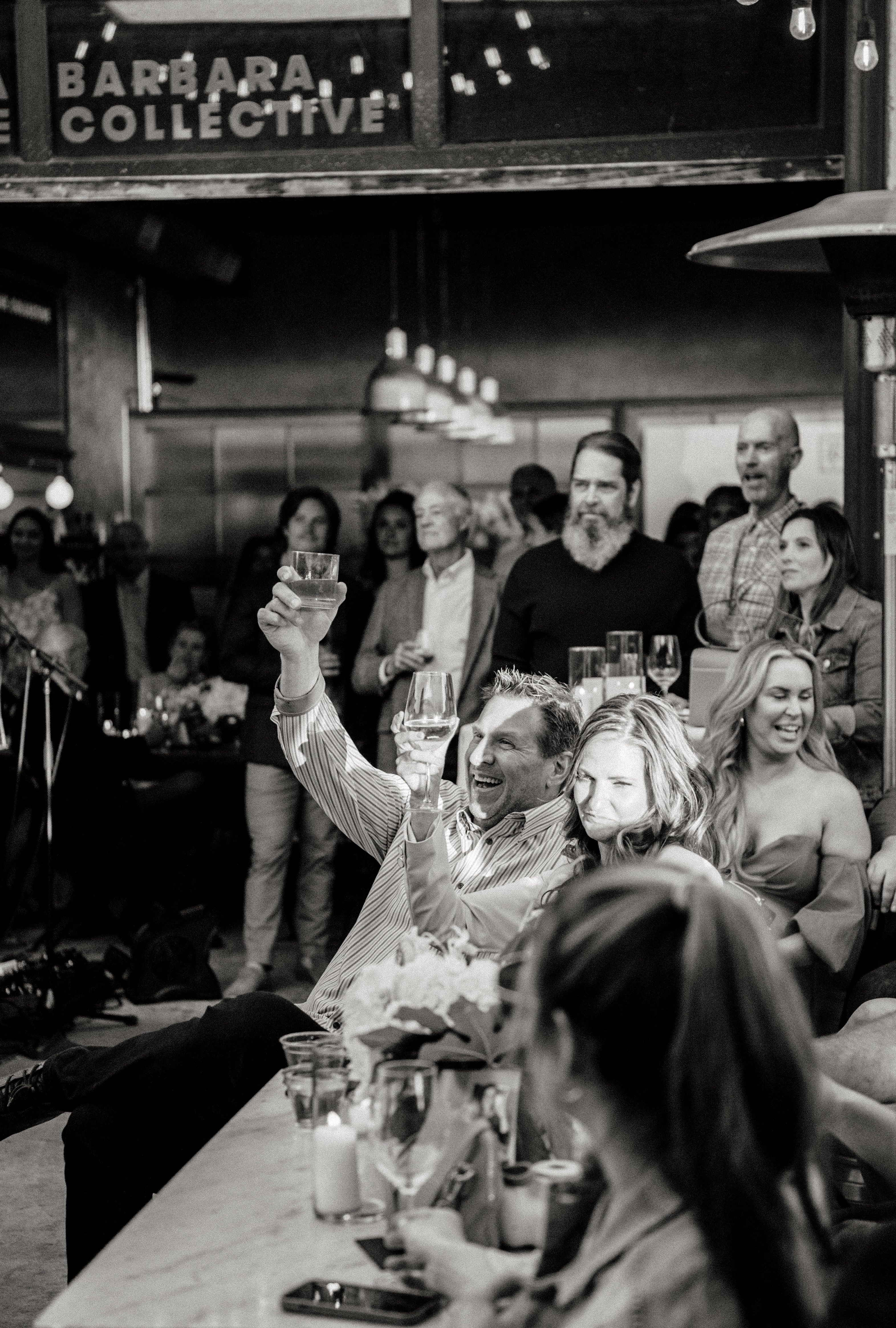 Black-and-white shot of a man raising his glass in a toast at a long table