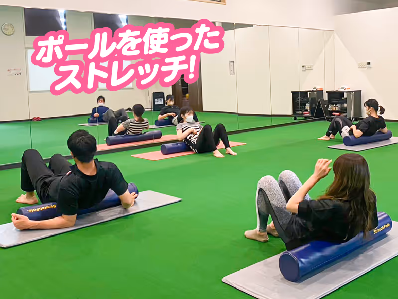 トレーニングマットの上でポールを使ってストレッチするマスク着用の男女。