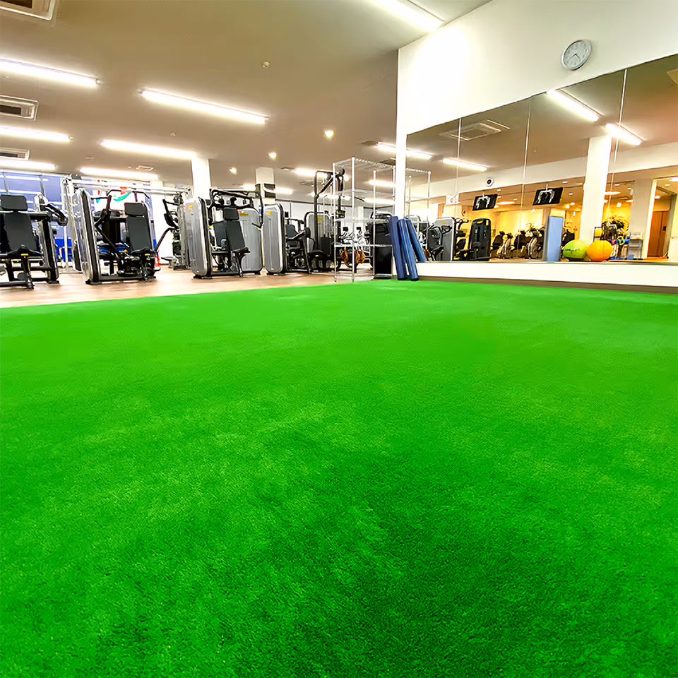 ジムのトレーニングマシンが並ぶ部屋の前に緑の人工芝エリアが広がっている。