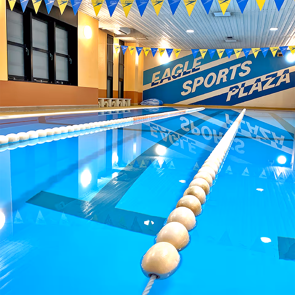屋内の水泳プールにはレーンロープが設置され、壁に'EAGLE SPORTS PLAZA'と大きく書かれている。