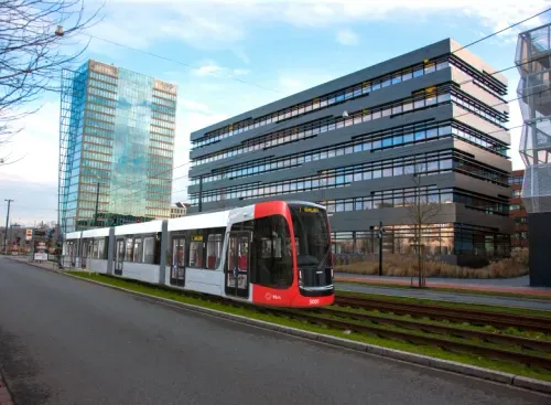 Modern red and white tram running on tracks beside a road near reflective glass office buildings.