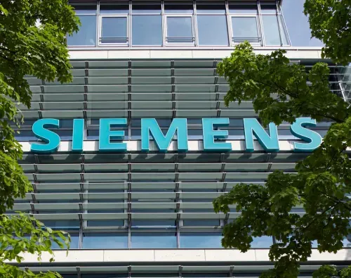 Siemens sign on a glass office building facade framed by green tree branches.
