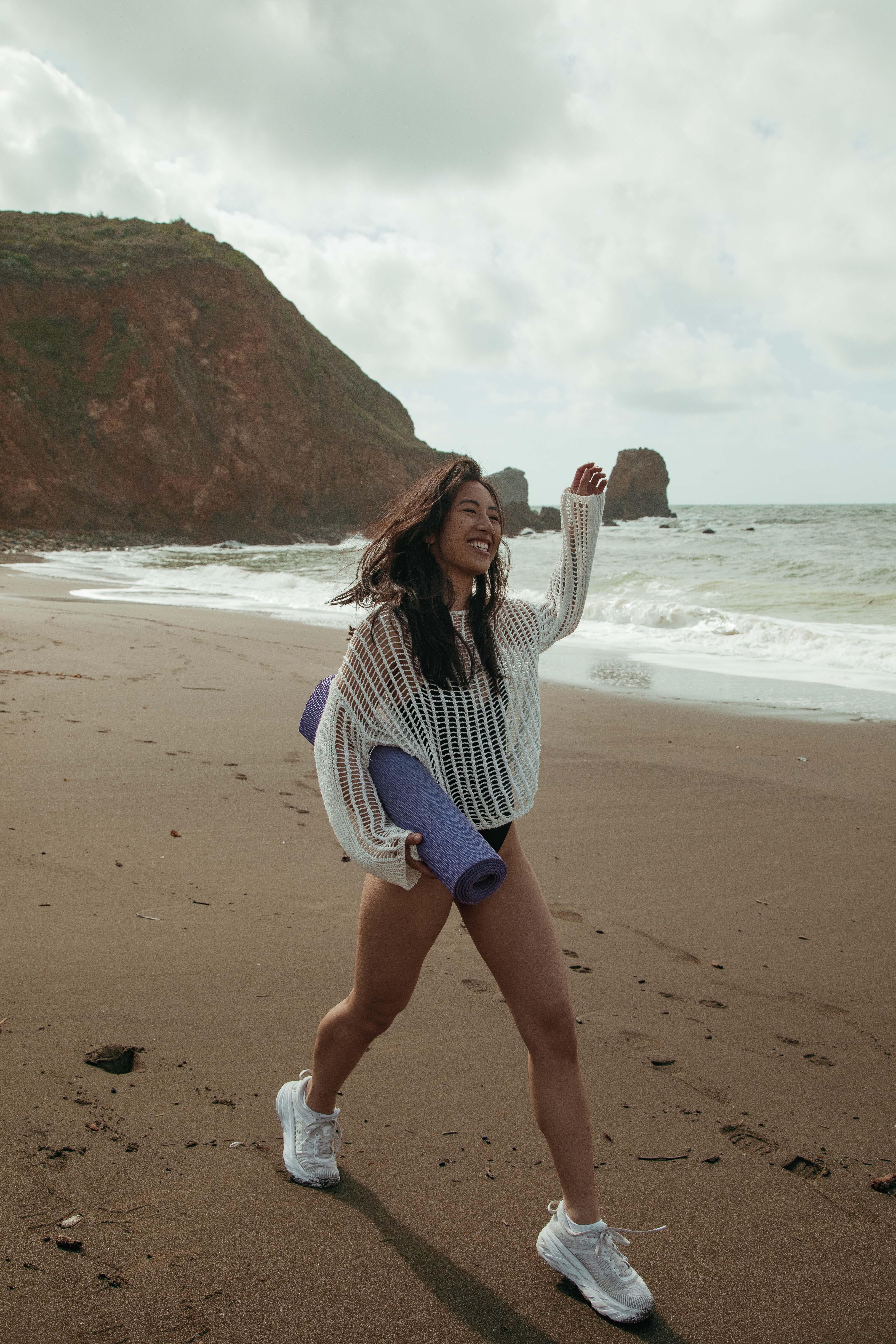 Picture of Sam smiling and walking along Pacifica beach holding a yoga mat.
