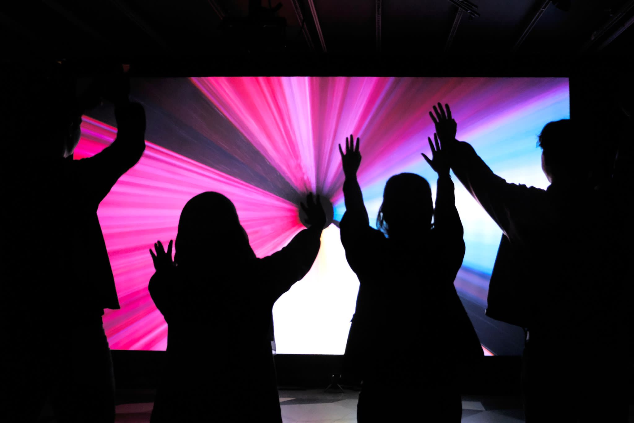 4 people raising their hands towards a projected graphics.