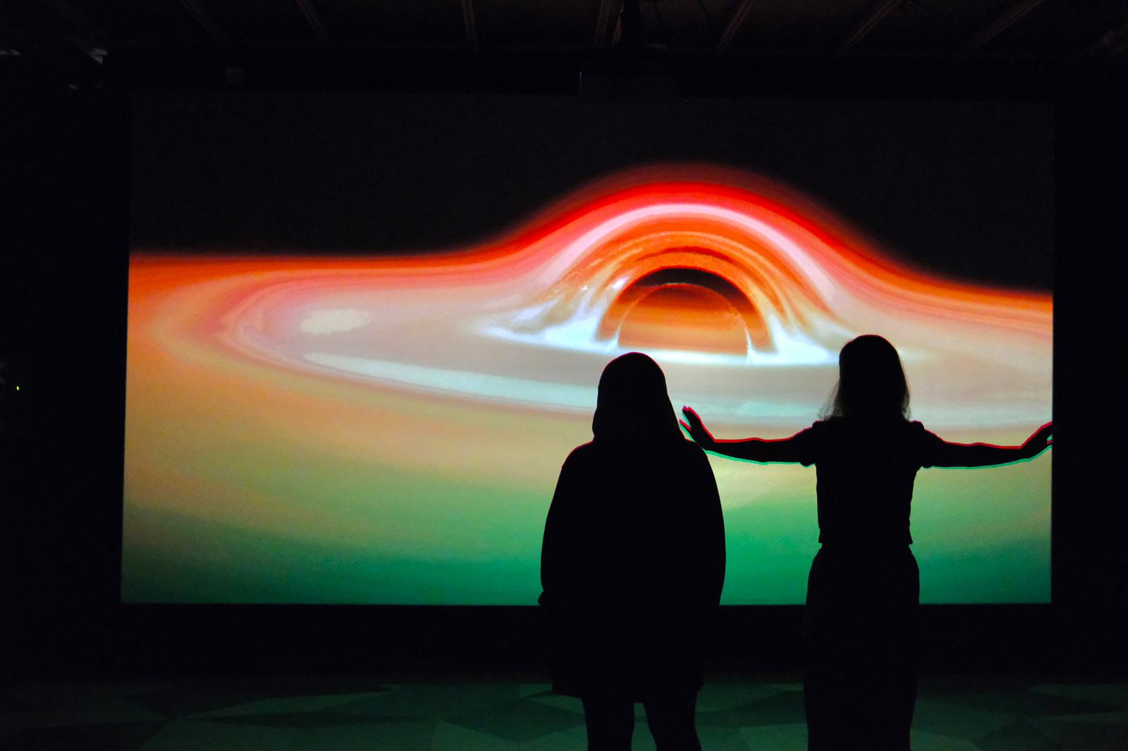 Two people in front of space projected blackhole.
