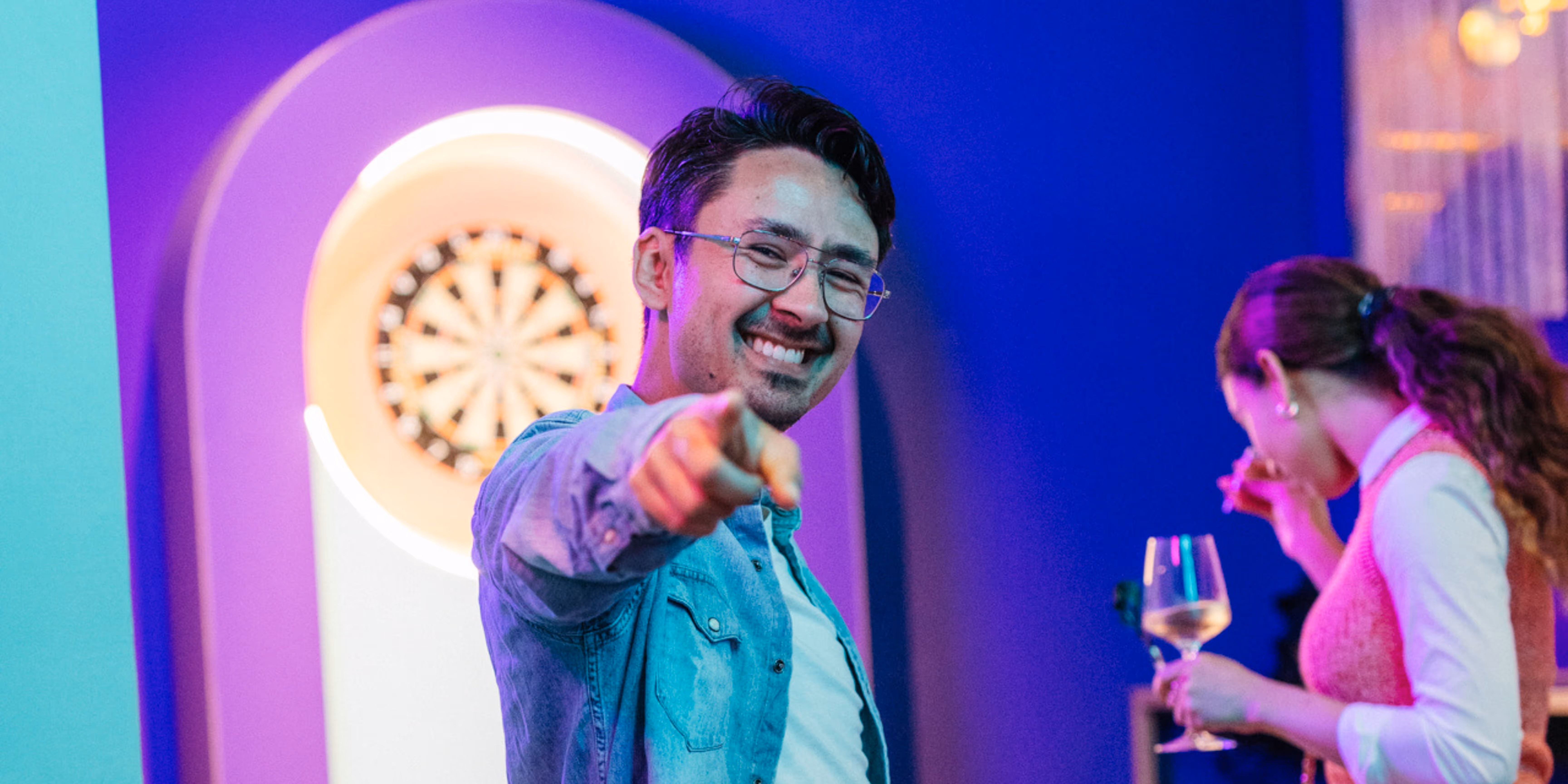 a person signing at the camera with a dart board in the back.