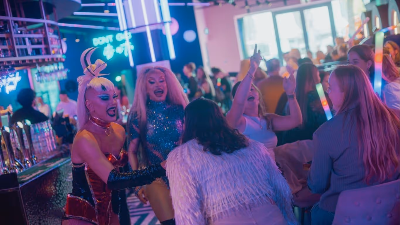 two dag queens interacting with a group of singing people.