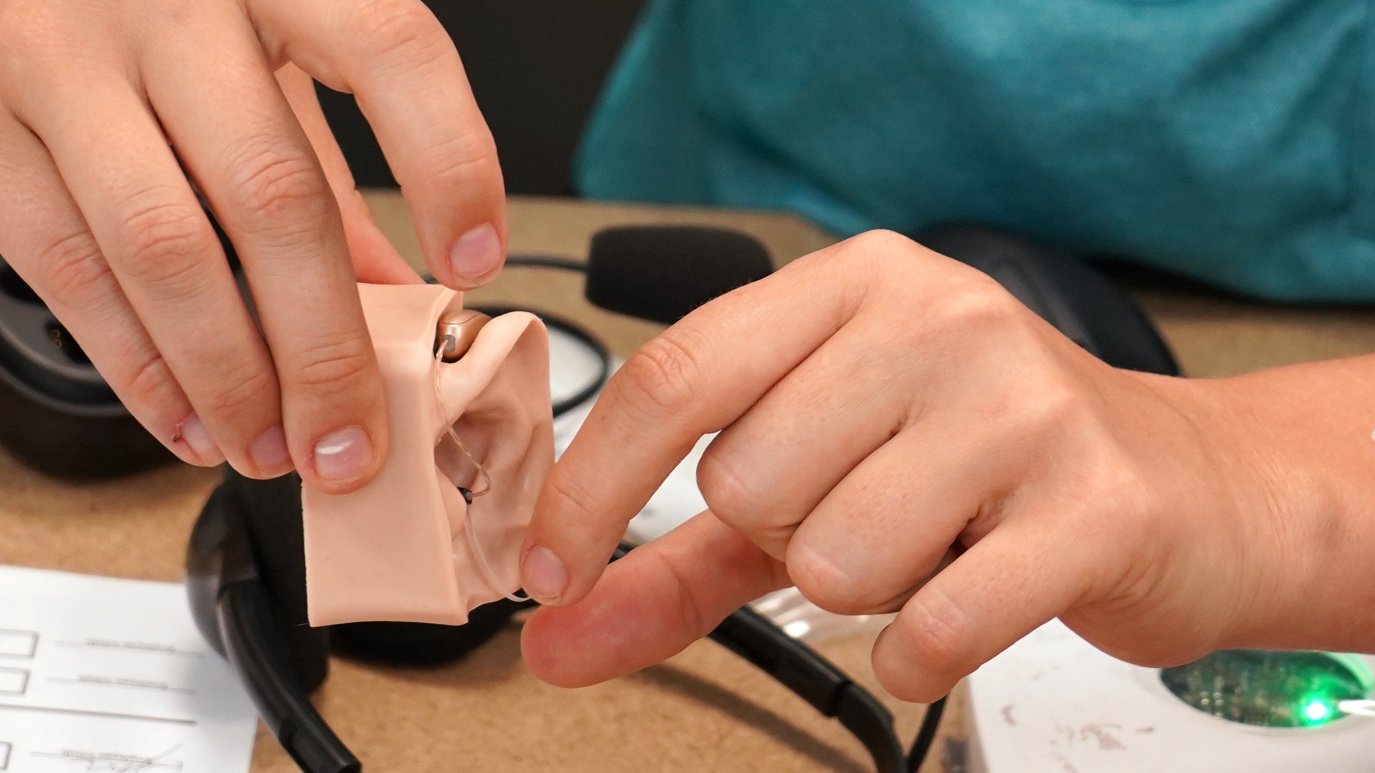 Close-up of hands placing a hearing aid into a silicone ear model