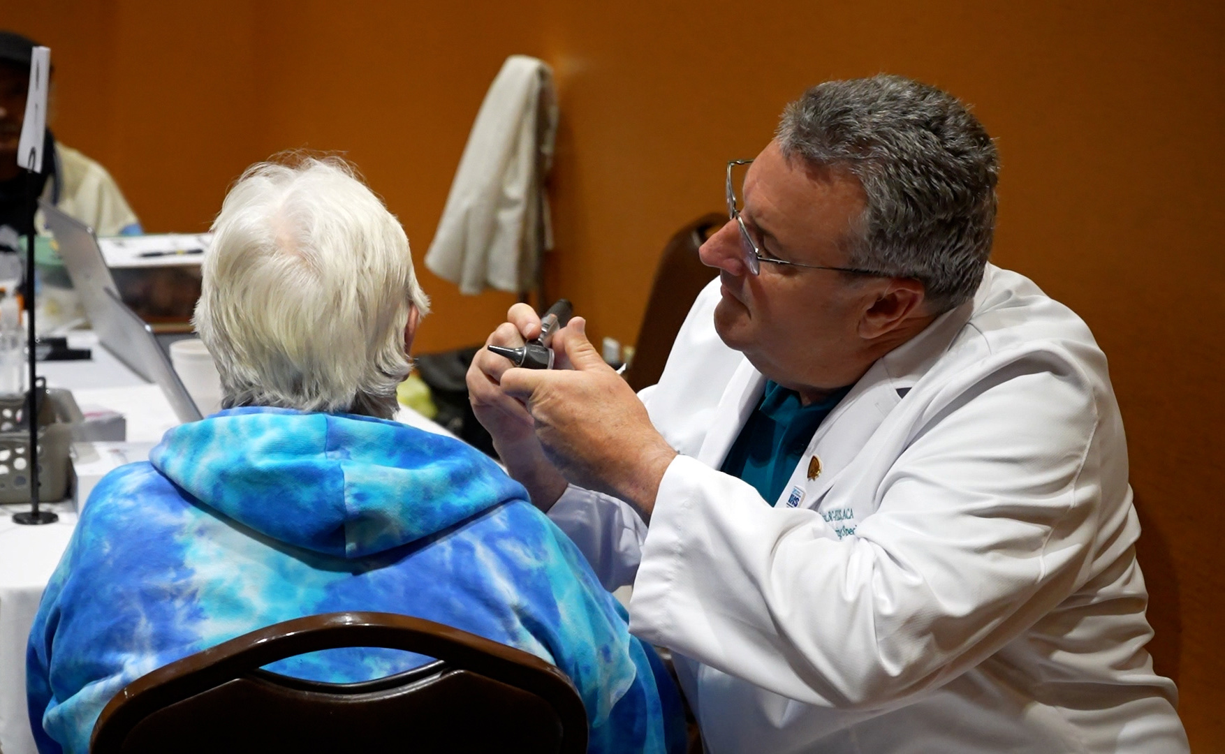 A hearing specialist examines a seated woman's ear during a screening