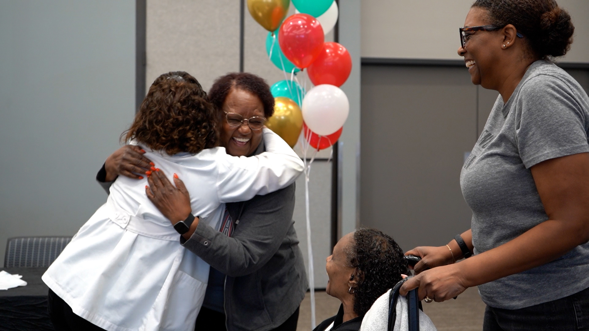 Two women embrace in celebration at a Gift of Sound event, balloons behind them
