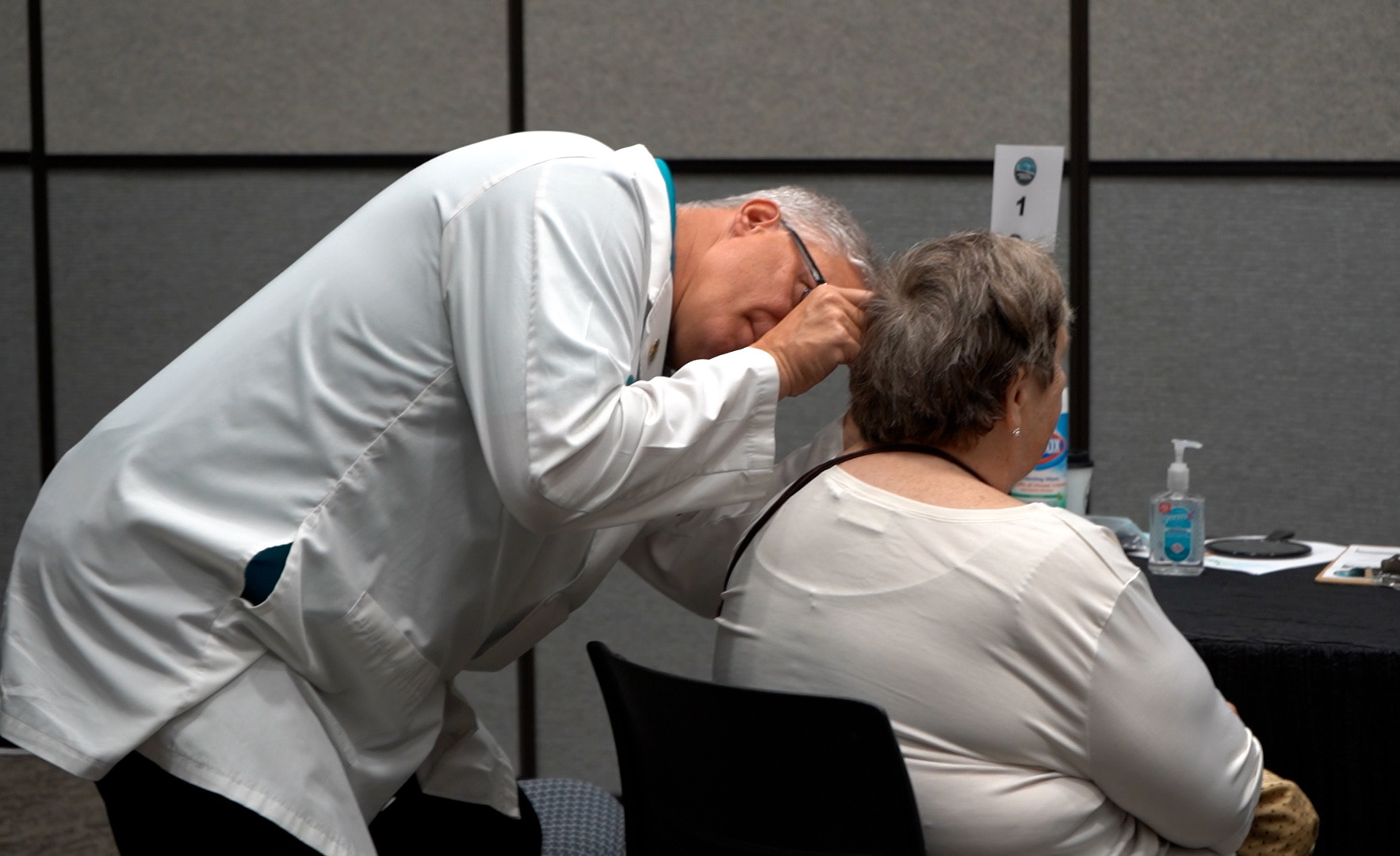 A specialist leans in to fit a hearing aid for a seated woman at an event