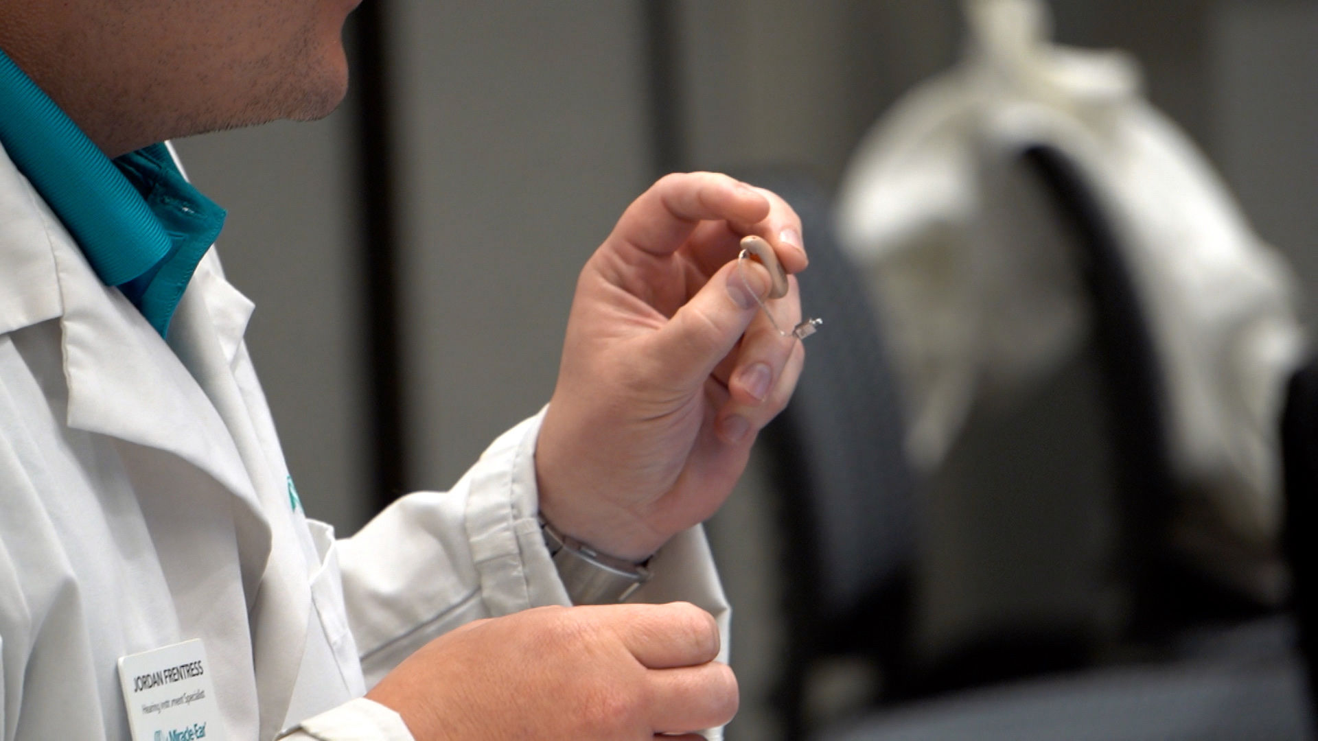 Close-up of a hearing specialist holding a small hearing aid between their fingers