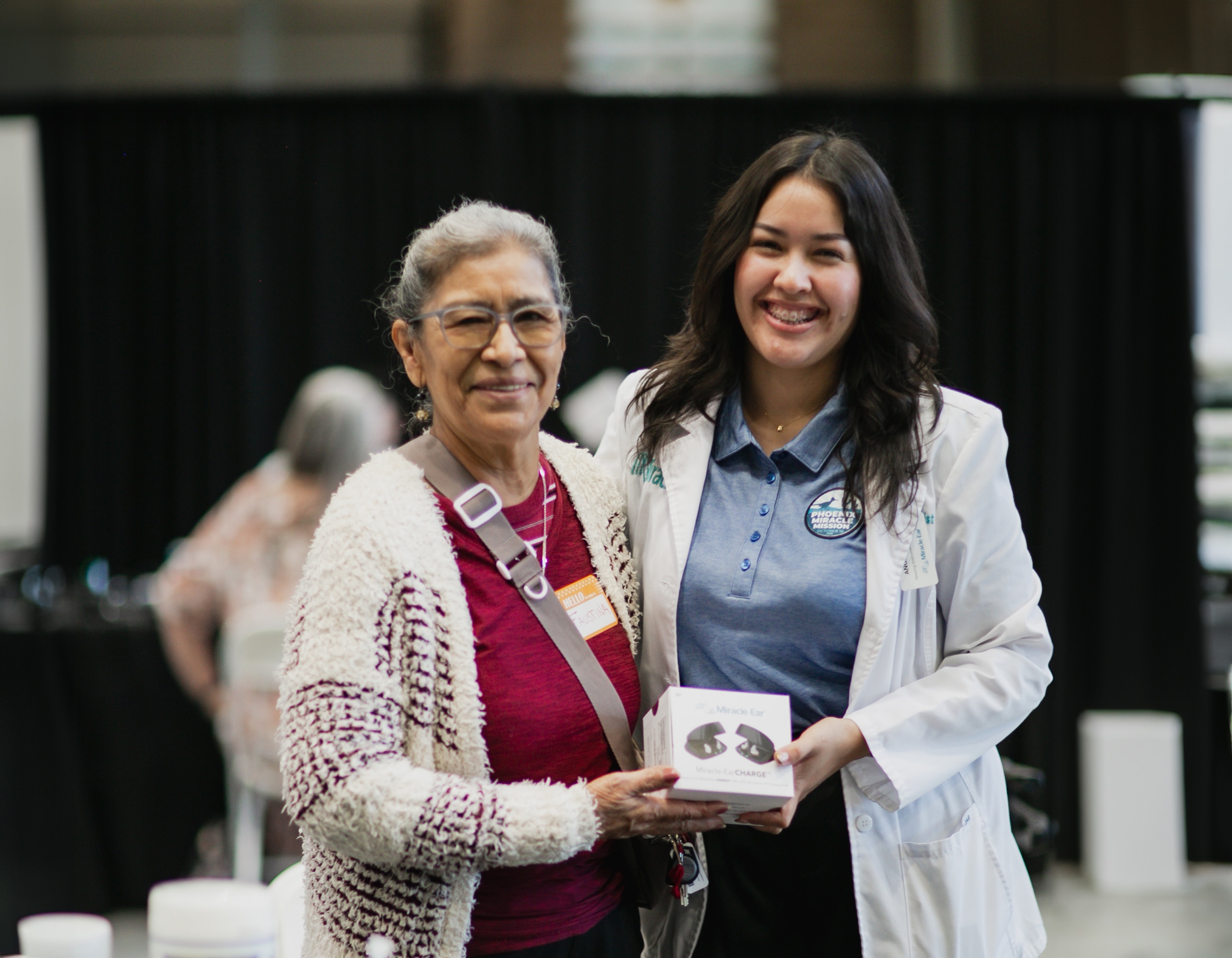 A recipient holds her new hearing aids beside a smiling Miracle-Ear specialist