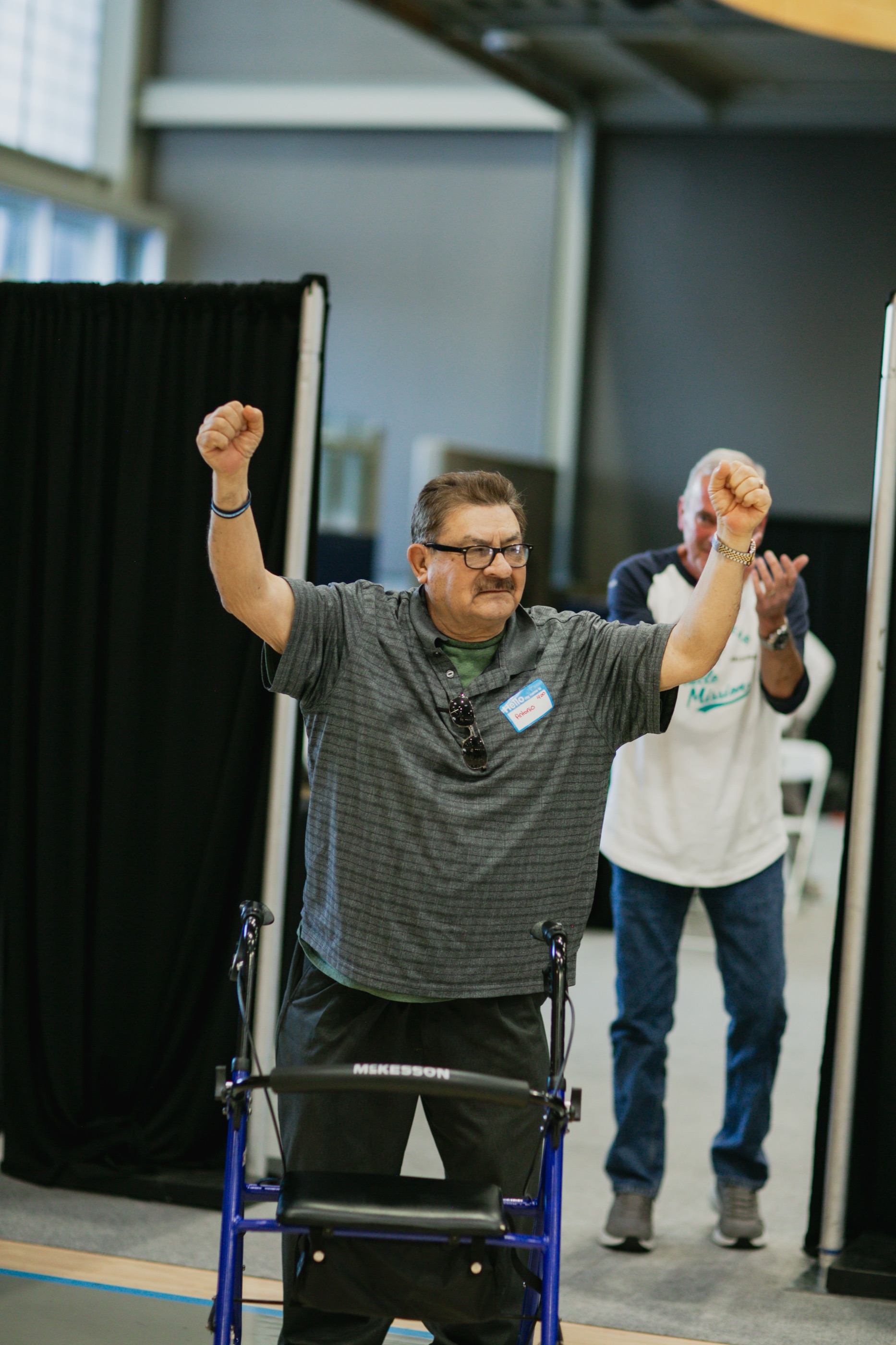 A man standing at a walker raises both fists in celebration after his fitting