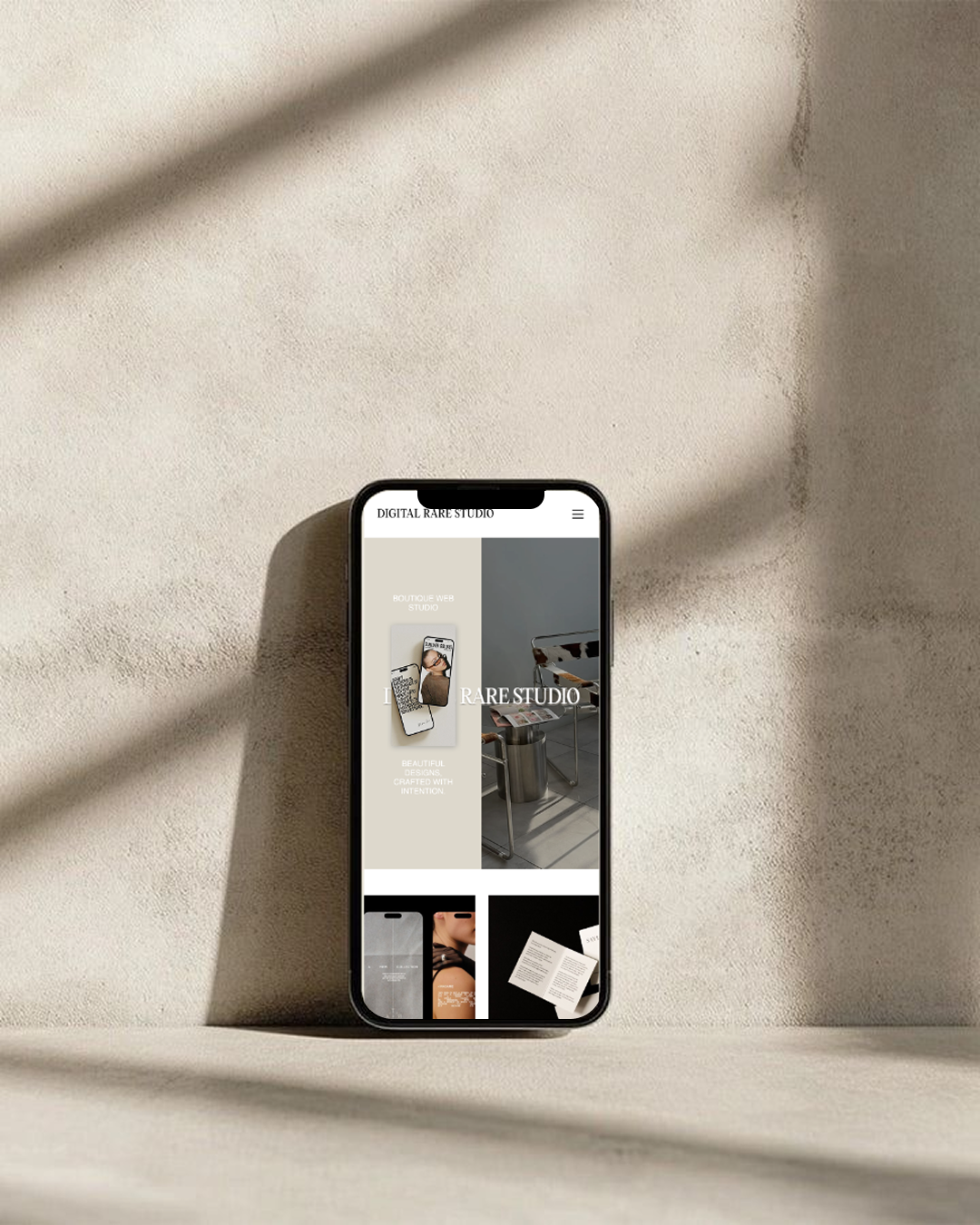 Smartphone leaning against a beige textured wall displaying a minimalist web studio website.