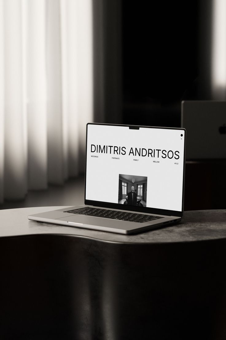 Laptop on a table showing a website with the name Dimitris Andritsos and a black-and-white photo.