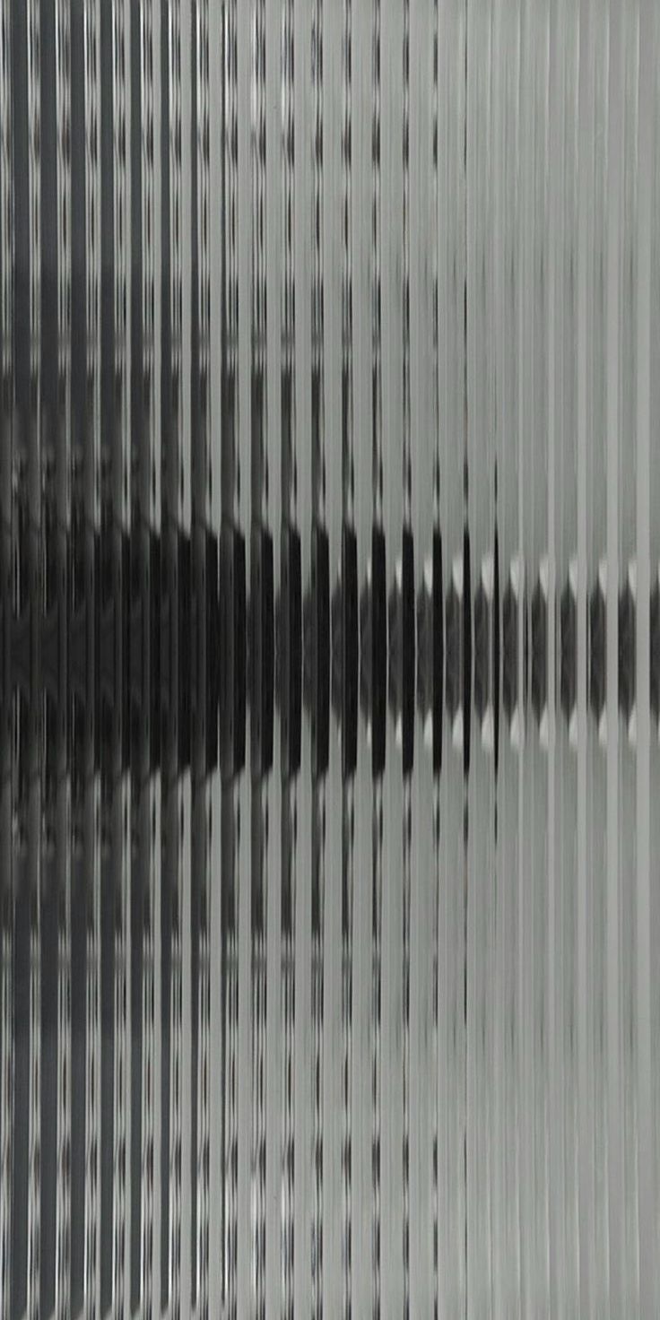 Close-up of vertically ribbed translucent textured glass with blurred stripe pattern behind it.
