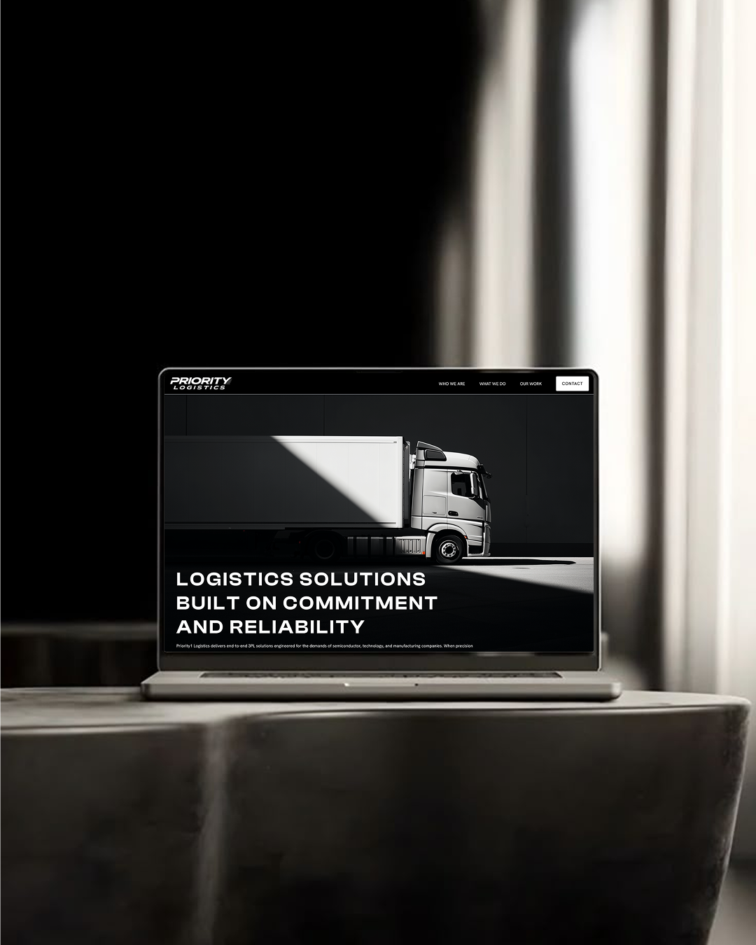Laptop on table shows Priority Logistics site with a white truck and text about commitment and reliability.
