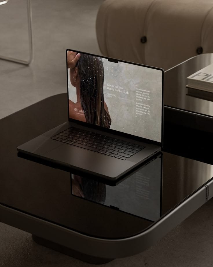 Laptop on a glossy black table displaying a woman's back with wet hair and text on the screen.