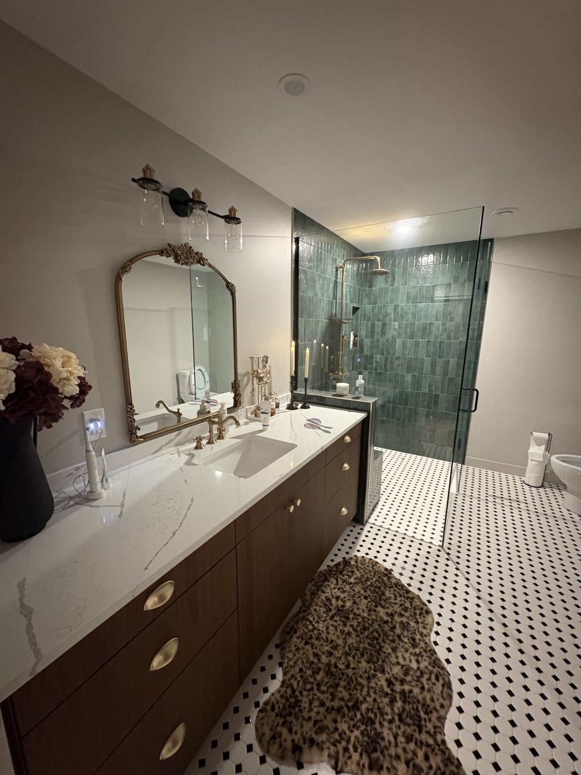 Spacious quiet luxury basement bathroom with long warm wood vanity, black-and-white mosaic tile floor and oversized green tiled walk-in shower.