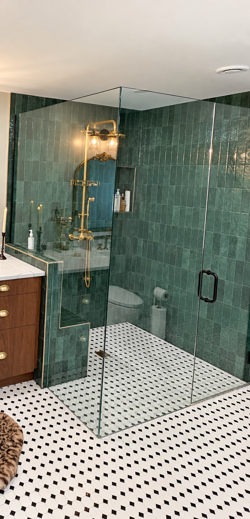 Oversized walk-in shower with frameless glass, rich green tile, built-in bench, recessed niche and warm brass fixtures.