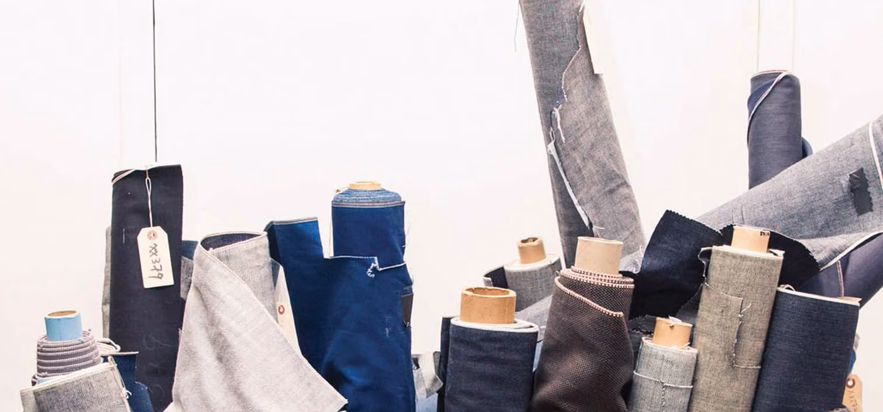 Several rolls of fabric in shades of blue, gray, and black standing upright with visible textures and tags against a light background.