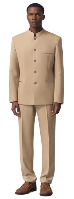 Man wearing a beige mandarin collar suit with brown buttons and brown shoes, standing facing forward.