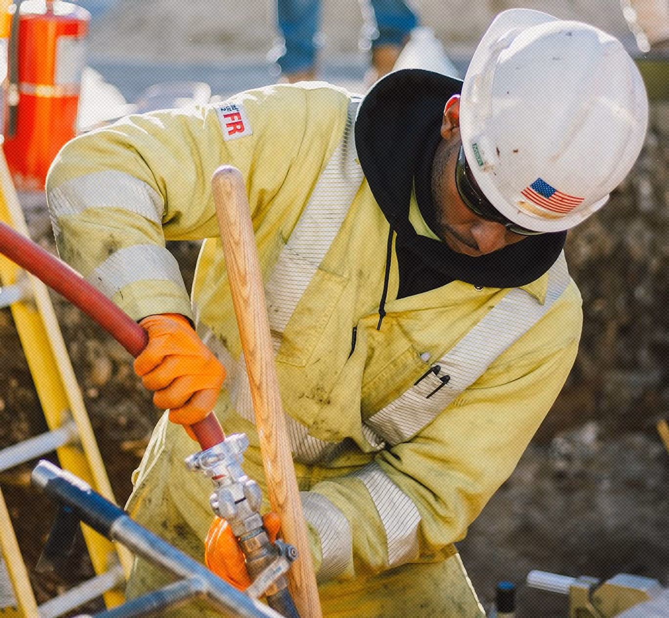 Construction worker in high-visibility jacket and hard hat operating equipment with red hose on a worksite.