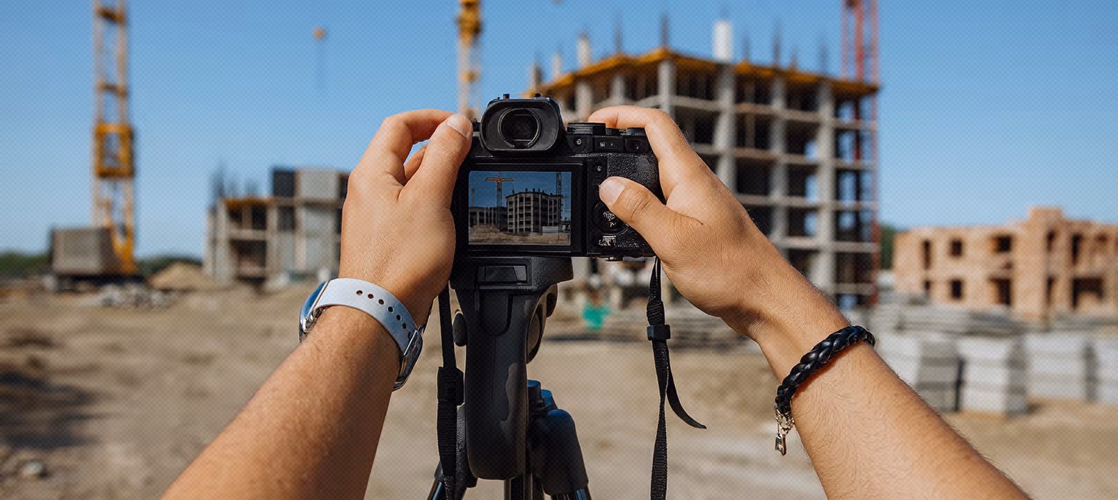 Person taking a photo of a construction site with a digital camera on a tripod.