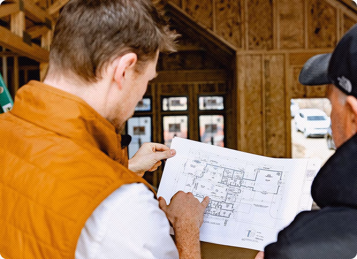 Two men inside a building under construction reviewing a blueprint floor plan.