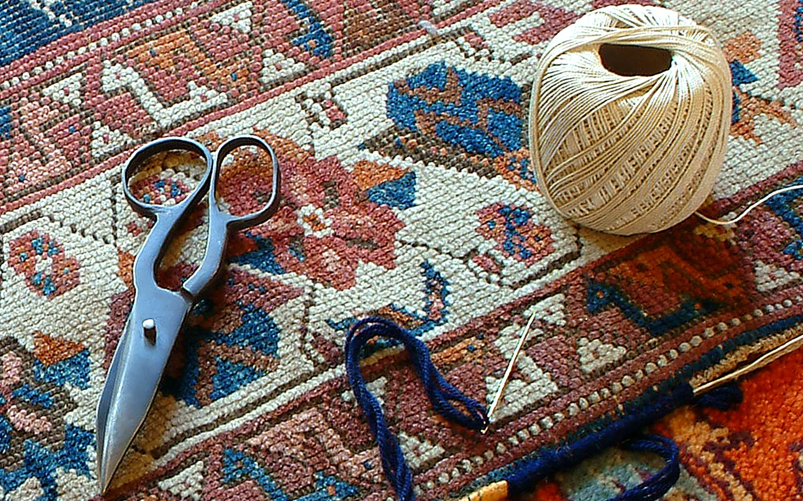 Ciseaux, fils et aiguille utilisés pour la restauration artisanale d'un tapis dans l'atelier Expo Kilim à Uccle.