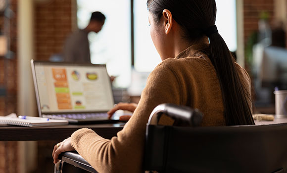 A woman in a wheel chair working at on a laptop in an office setting