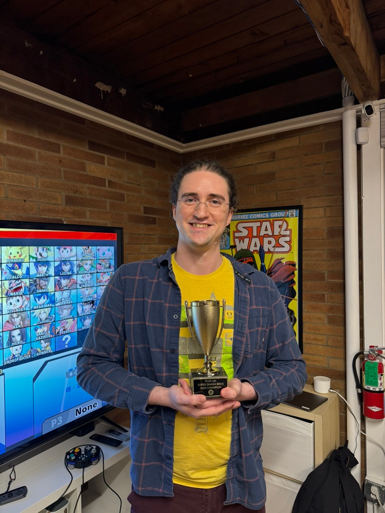 Merlin Benneth holding trophy for winning PLUS QA's 2024 Super Smash Brothers competition