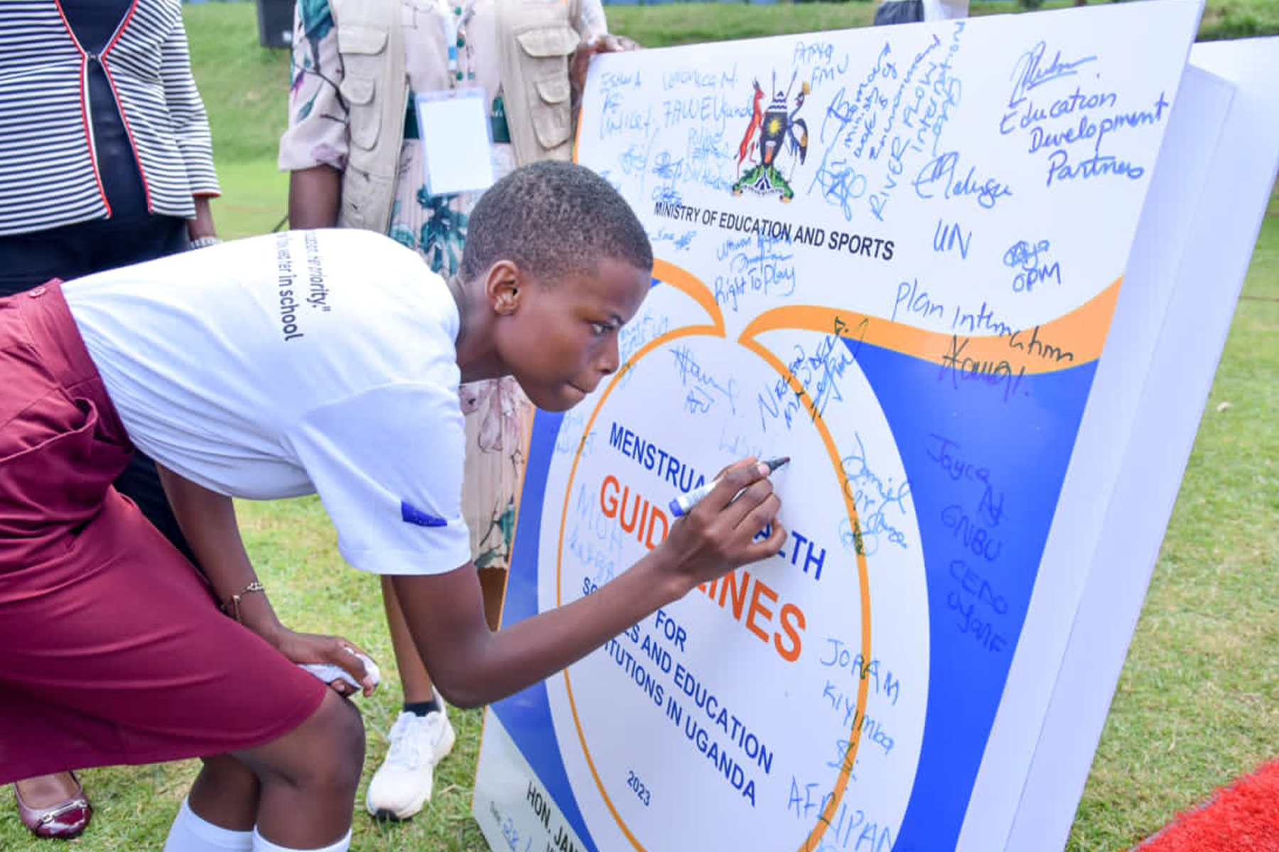 A women bends down to sign a poster announcing new menstrual health guidelines by the Ugandan Ministry of Education and Sports.